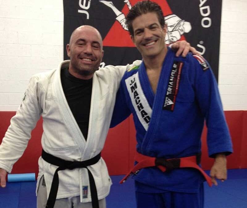 Joe Rogan and a Brazilian Jiu Jitsu practitioner posing together in martial arts uniforms, showcasing their passion for BJJ training.